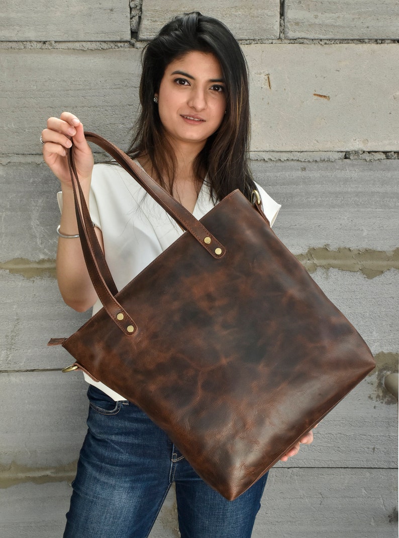 K&ouml;nnte beinhalten: Eine braune Ledertasche mit Rei&szlig;verschluss und zwei Henkeln. Die Tasche hat einen Used-Look und ist aus hochwertigem Leder gefertigt.