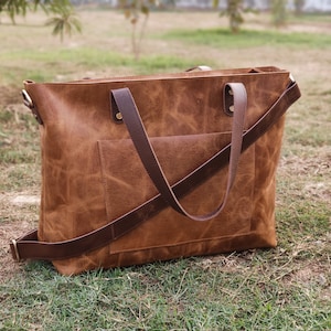 May include: A brown leather tote bag with a long strap and two shorter handles. The bag has a front pocket and a distressed look.