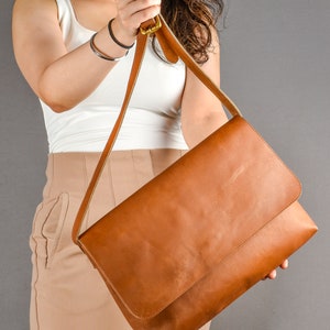 May include: A brown leather messenger bag with a long adjustable strap. The bag has a flap closure and a smooth, textured surface.
