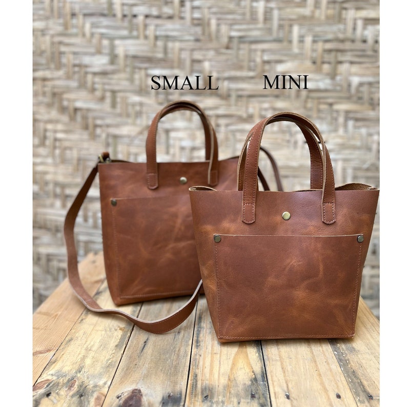 The mini leather tote bag comes with a button closure to secure your belongings. The small leather purse has a large outside pocket with brass rivets in its top two corners. The inside of the bag has two pockets to keep your phone and wallet.