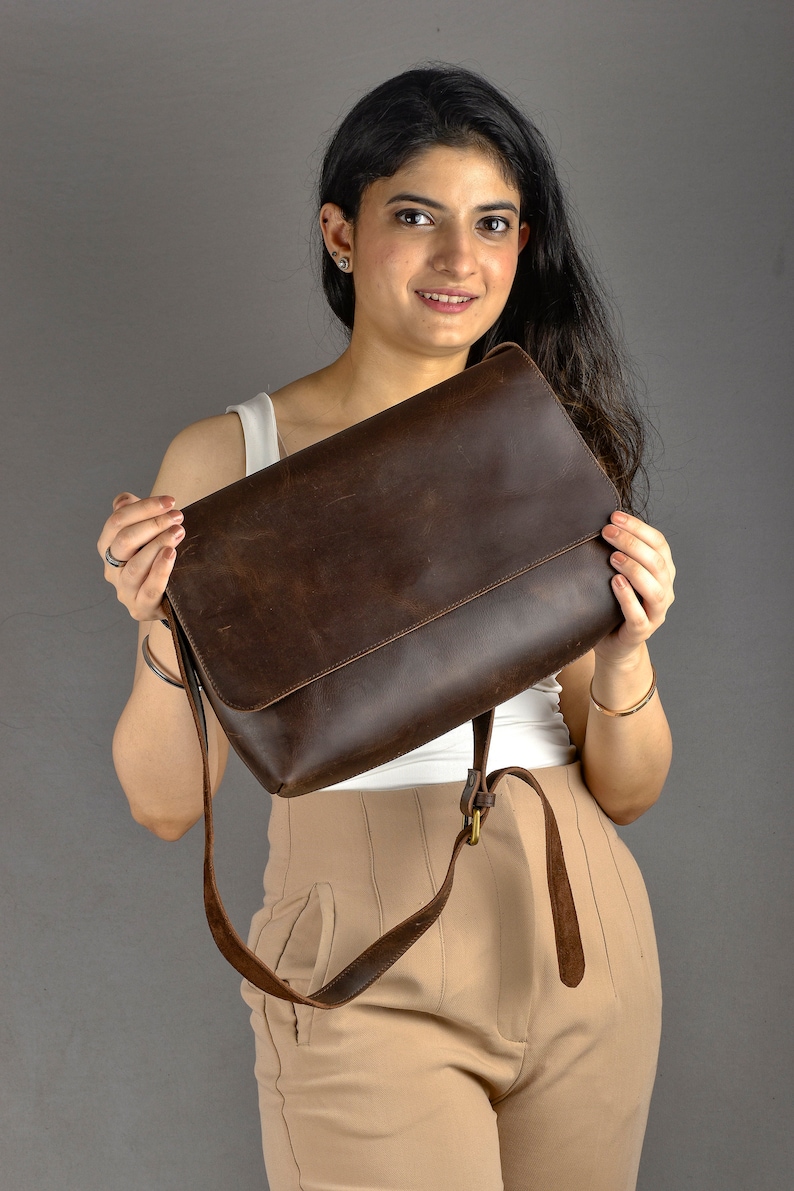 May include: A brown leather messenger bag with a long adjustable strap. The bag has a flap closure and a single compartment.