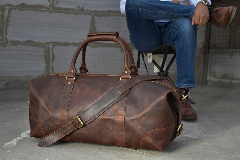 Pu&ograve; includere: Una borsa da viaggio in pelle marrone con una lunga tracolla e due manici superiori. La borsa ha un aspetto vissuto ed &egrave; realizzata in pelle di alta qualit&agrave;.