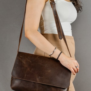 May include: A brown leather messenger bag with a long strap. The bag has a flap closure and a distressed look.