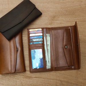 Puede incluir: Dos carteras de cuero, una marr&oacute;n y otra negra, est&aacute;n abiertas y dispuestas sobre una superficie de madera. La cartera marr&oacute;n tiene m&uacute;ltiples ranuras para tarjetas y un portafolios, mientras que la cartera negra tiene un dise&ntilde;o m&aacute;s simple.