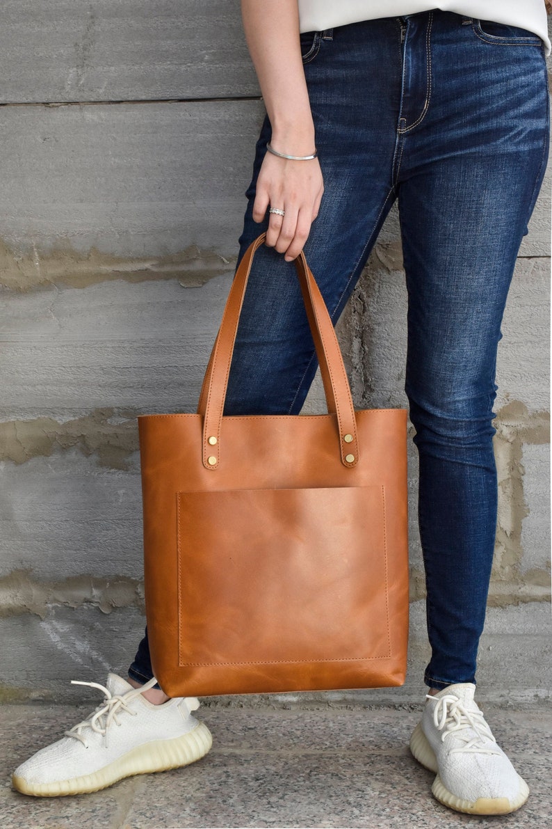 The leather tote bag for women comes with optional zipper and crossbody strap to wear across body. Its the perfect work tote purse with a large exterior pocket and two interior pockets. Tote bag can hold laptop and comes in two colours black and tan.