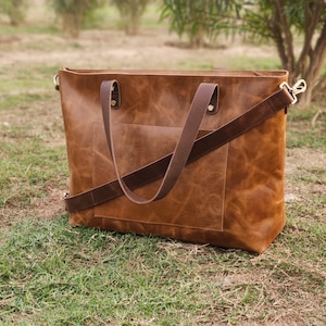 May include: A brown leather tote bag with a long strap and a front pocket. The bag has a distressed look and is made of high-quality leather.