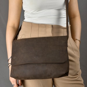 May include: A brown leather messenger bag with a long strap worn over the shoulder. The bag has a flap closure and a single compartment.