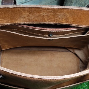 K&ouml;nnte beinhalten: Das Innere einer braunen Ledertasche mit Rei&szlig;verschlussfach und braunem Stofffutter.