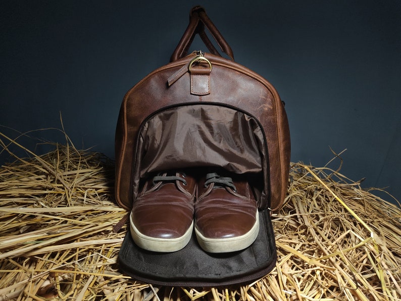 May include: A brown leather duffel bag with a pair of brown shoes inside. The bag has a top handle and a gold-colored zipper pull. The shoes have white soles and black laces. The background is a dark blue.