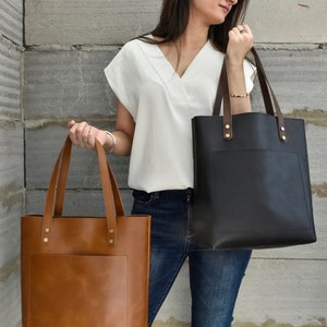 The leather bag comes in two colours tan and black. The model is holding both the colours to show the difference between both the colours.