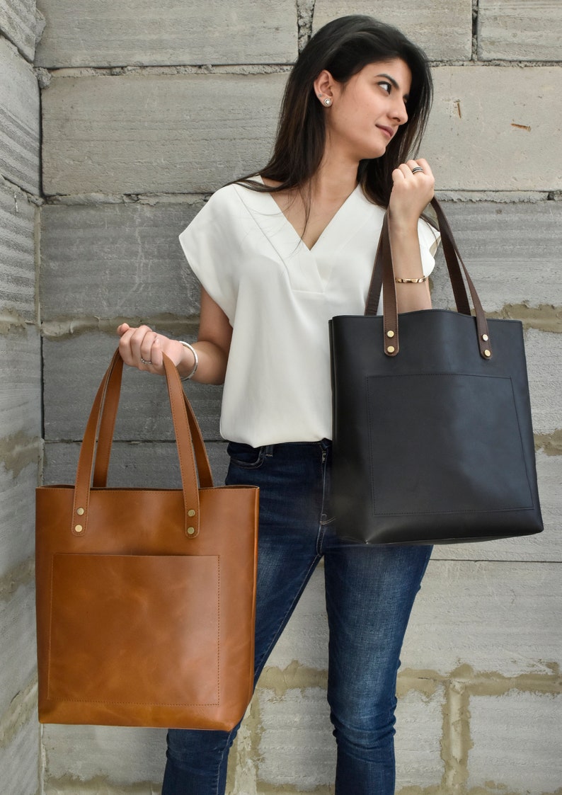 The leather bag comes in two colours tan and black. The model is holding both the colours to show the difference between both the colours.