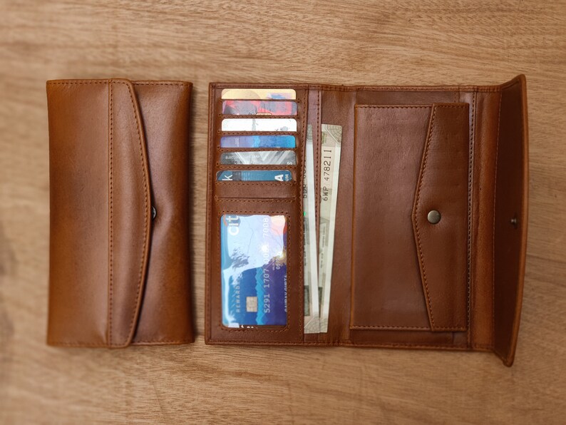 May include: A brown leather wallet with multiple card slots and a billfold. The wallet is open and has several cards and bills inside.