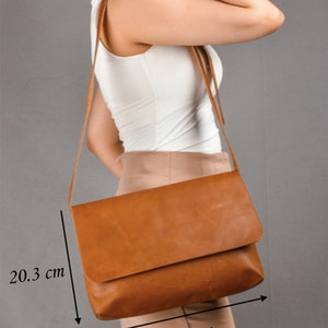 May include: A brown leather crossbody bag with a flap closure. The bag measures 33 cm wide and 20.3 cm tall.