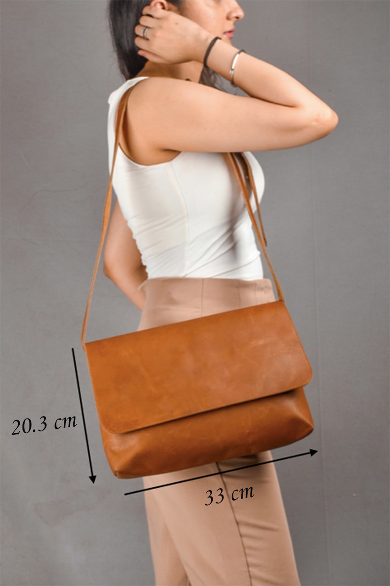 May include: A brown leather crossbody bag with a flap closure. The bag measures 33 cm wide and 20.3 cm tall.