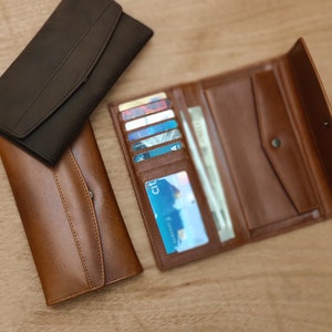May include: Two leather wallets, one brown and one black. The brown wallet is open, showing multiple card slots and a money compartment.