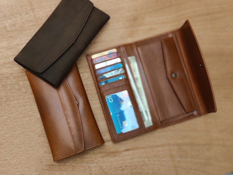 May include: Two leather wallets, one brown and one black. The brown wallet is open, showing multiple card slots and a money compartment.