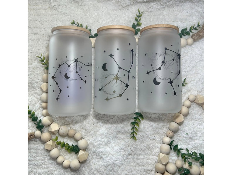 May include: Three frosted glass jars with bamboo lids, each featuring a different constellation design with a crescent moon and stars. The constellations are Aquarius, Virgo, and Gemini. The jars are labelled "CREATIONS BY KRISTINE" and "KRISTINE DESIGNS".