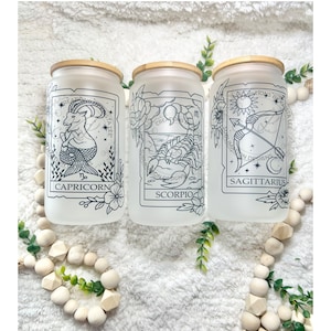 May include: Three frosted glass jars with bamboo lids, each featuring a different zodiac sign: Capricorn, Scorpio, and Sagittarius. The signs are depicted in black line art with floral accents.