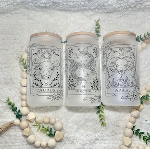 May include: Three frosted glass jars with wooden lids, each featuring a different zodiac sign: Taurus, Pisces, and Aries. The signs are depicted in black line art with floral accents.