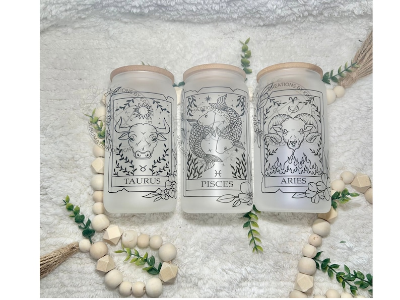 May include: Three frosted glass jars with wooden lids, each featuring a different zodiac sign: Taurus, Pisces, and Aries. The signs are depicted in black line art with floral accents.