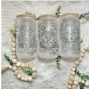 May include: Three frosted glass jars with bamboo lids, each featuring a different zodiac sign: Leo, Gemini, and Cancer. The jars are decorated with black line drawings of the zodiac symbols and have a white background.