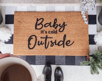 May include: A brown coir doormat with the text "Baby it's cold outside" in black cursive lettering.
