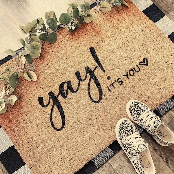 Puede incluir: Una alfombra de coco marrón con el texto "yay! it's you" en escritura negra. La alfombra está sobre una superficie a cuadros en blanco y negro.