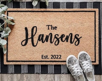 May include: A brown coir doormat with black trim and the text "The Hansens Est. 2022" in black lettering.