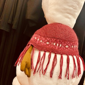 May include: A white plush snowman with a red knitted scarf with white trim and tassels. The scarf has a fringe around the bottom.