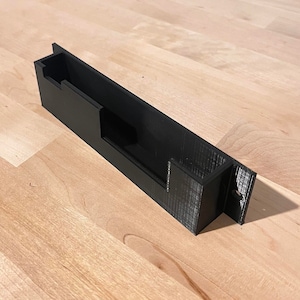 May include: A black plastic wall mount with a rectangular cutout for holding a small object.