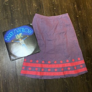 May include: A purple skirt with a pink and white polka dot trim. The skirt is made of a soft, lightweight fabric and has a flowy silhouette.