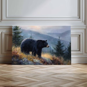 Könnte beinhalten: Ein rechteckiger Wandkunstdruck, der einen Schwarzbären auf einem felsigen, grasbewachsenen Grat zeigt. Der Hintergrund zeigt eine neblige Berglandschaft mit immergrünen Bäumen unter einem weichen, dunstigen Himmel in Naturtönen.
