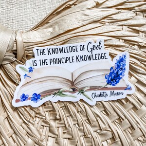 May include: A white sticker with a quote about the knowledge of God, "The knowledge of God is the principle knowledge." The quote is attributed to Charlotte Mason. The sticker features a watercolor illustration of an open book with blue flowers.