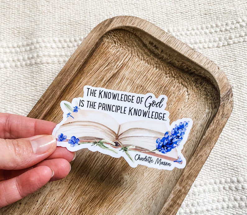 May include: A white sticker with an open book and blue flowers. The sticker has the text "The knowledge of God is the principle knowledge." and "Charlotte Mason".