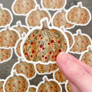 May include: A collection of fall-themed pumpkin stickers with a watercolor design. The pumpkins are decorated with a pattern of small red mushrooms and green leaves.