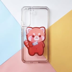 May include: Transparent phone case with a cartoon red panda holding a knife. The red panda has a sad expression and is set against a colourful background. The text "bakadreams" is at the bottom of the case.