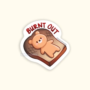 May include: A sticker featuring a cartoon bear lying on a piece of toast. The text "BURNT OUT" is written in red above the bear. The sticker has a white border and the @bakadreams logo.