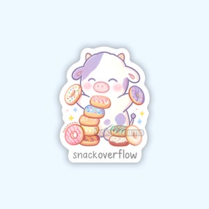 May include: A sticker featuring a cartoon cow with purple spots and horns, holding a stack of donuts. The donuts have various toppings and colors. The sticker has the text "snackoverflow" at the bottom.