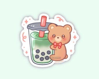 May include: A sticker featuring a cute cartoon bear with a red bow, next to a green bubble tea with black tapioca pearls. The sticker has a white border and the text "bakadreams". The background is a light green color.