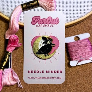 K&ouml;nnte beinhalten: Ein schwarzer Rabe mit einer Hexenm&uuml;tze sitzt auf einem goldenen Halbmond mit wei&szlig;en Sternen. Die Nadel ist auf einer wei&szlig;en Karte mit dem Text "FarOut Handmade" und "Needle Minder" mit der Website "farouthandmade.etsy.com".