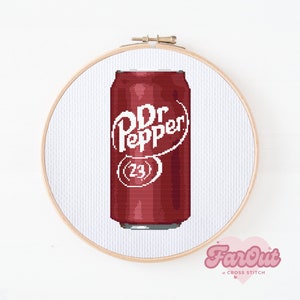May include: A red and white Dr Pepper can cross stitch pattern. The can is in a wooden embroidery hoop.