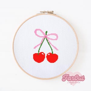 May include: A cross stitch pattern of two red cherries with green stems and a pink bow on a white background.