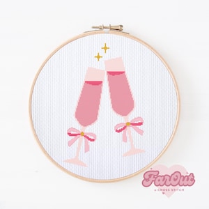 May include: A cross stitch pattern of two pink champagne glasses with gold bows, on a white background.