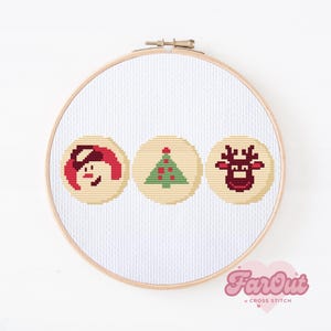 Puede incluir: Un aro de bordado blanco con tres diseños de galletas de Navidad bordados en punto de cruz: un muñeco de nieve, un árbol de Navidad y un reno. Los diseños son en rojo, verde y marrón.