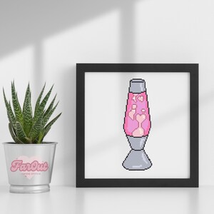 Op de afbeelding: Een ingelijst kruissteekpatroon van een roze lava lamp met harten erin. De lijst is zwart en de achtergrond is wit.