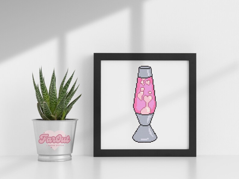 Op de afbeelding: Een ingelijst kruissteekpatroon van een roze lava lamp met harten erin. De lijst is zwart en de achtergrond is wit.