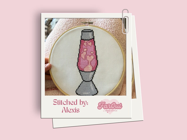 Op de afbeelding: Een kruissteek van een roze en witte lava lamp in een houten borduurring. De tekst "Stitched by: Alexis FarOut Cross Stitch" staat onder de ring.