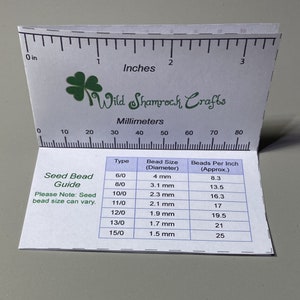 May include: A white card with a green shamrock logo and the text "Wild Shamrock Crafts". The card has a ruler with inches and millimeters marked. The card also has a table with seed bead sizes and beads per inch.