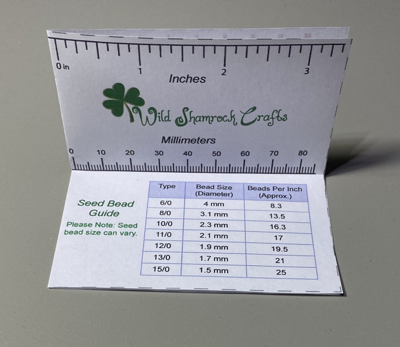 May include: A white card with a green shamrock logo and the text "Wild Shamrock Crafts". The card has a ruler with inches and millimeters marked. The card also has a table with seed bead sizes and beads per inch.