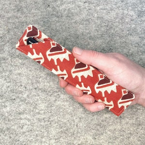May include: A red and white patterned fabric pen case with a black pen inside.